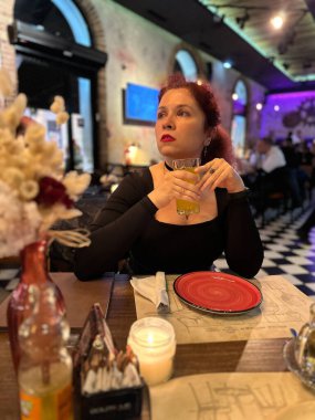 Milenyum kadını, canlı bir restoranda, kırmızı tabağı ve sıcak mum ışığı olan bir masada keyifli bir akşamın tadını çıkarıyor. Atmosfer, modern ve rahat iç tasarımın bir karışımı olan gecedir.