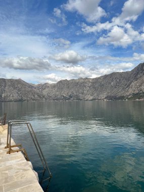 Huzurlu dağ manzarası, resim gibi bir gökyüzünün altındaki dingin gölü yansıtıyor. Görüntü, doğal güzelliğin ve vahşi doğadaki huzurun özünü yakalıyor.