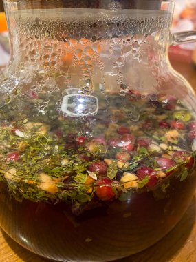 Modern bir kafede, ahşap bir tepsinin üzerinde bitki çaydanlığının olduğu cam bir çaydanlık. Çevre aydınlatma ve çağdaş dekor sıcak ve davetkar bir atmosfer yaratır.