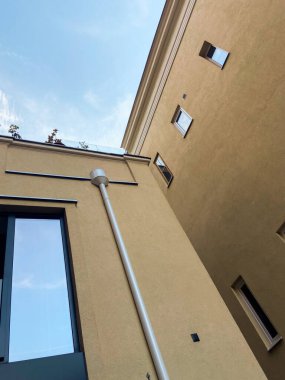 Parlak mavi gökyüzüne karşı iki modern bej binanın kesişimine bakıyorum. Mimari ve açık gökyüzü arasındaki zıtlığı vurgulayan minimalist şehir manzarası.