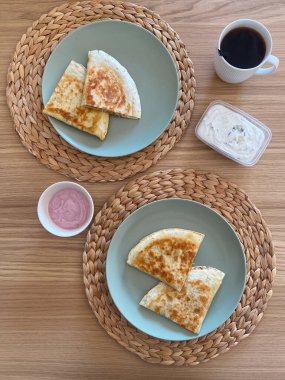 Quesadillas, dokuma tabaklarına yerleştirilmiş yuvarlak tabaklarda servis edilir. Mutfak lezzeti sunar. Tortillaların dokusu ve altın tonu rahatlatıcı bir yemek deneyimi yaşatıyor. Meksika mutfağı.