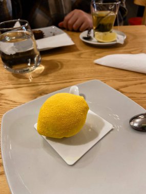 Samimi bir kafe ortamında beyaz bir tabakta servis edilen gerçekçi limon şekilli tatlı. Yaradılış, gelişigüzel bir yemek deneyiminin ortasında bir hoşgörü anına davet eder..