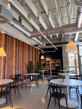 Gösterişli mobilyalar, ahşap panel duvarlar ve eşsiz ışıklandırmalı endüstriyel tavan tasarımı olan modern kafe iç mimarisi.