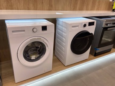 Modern çamaşır makineleri bir elektronik mağazasında sergileniyor, son model modeller şık tasarımlar ve gelişmiş özelliklerle sergileniyor. Parlak ışıkların altında, makineler,