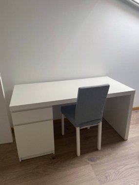 Minimalist çalışma alanı, beyaz bir masa ve ahşap zeminde gri bir sandalye. Basit tasarım üretkenlik ve odak için mükemmel temiz ve düzenli bir ortam sunar.