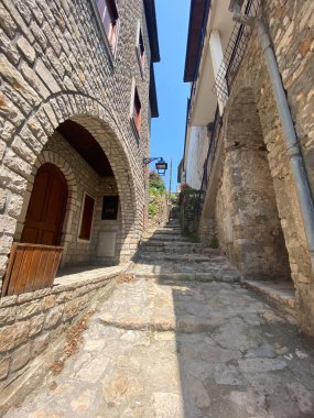 Aydınlık taş sokak, parlak mavi gökyüzünün altındaki geleneksel taş binaların arasına dik bir şekilde tırmanıyor. Davetkar merdiven tarihsel mimari tarafından çerçevelenmiş, zamansız cazibe ve sükunet hissi uyandırıyor..