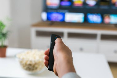 Afrikalı Amerikalı bir kadın gri bir kanepeye oturup film izlerken veya internetten film izlerken bir kase patlamış mısırın tadını çıkarıyor. Modern bir evde rahat ve rahatlatıcı bir eğlence anı. Bağlantı