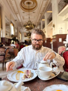 Milenyum adamı klasik dekorlu lüks bir kafede zarif bir çay molası veriyor. Lüks restoran güzel sofra takımı ve bir dilim pasta ile donatılmış, zamansız ve rafine bir atmosfer..