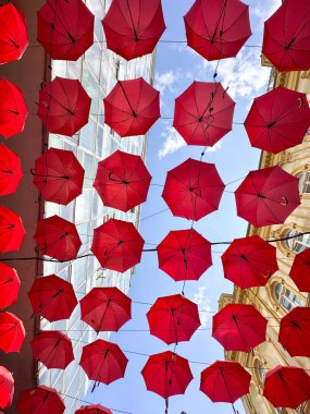 Açık mavi gökyüzüne asılı kırmızı şemsiyeler, kaprisli ve sanatsal atmosfer. Yaratıcılığın ve kentsel mimarinin birleşimi, açık hava restoranı ve otelin dış tasarımı