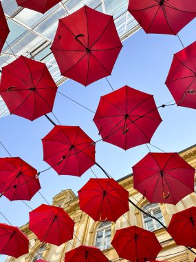Açık mavi gökyüzüne asılı kırmızı şemsiyeler, kaprisli ve sanatsal atmosfer. Yaratıcılığın ve kentsel mimarinin birleşimi, açık hava restoranı ve otelin dış tasarımı