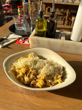 Sıcak güneş ışığı altında rendelenmiş peynirle kaplanmış bir kase makarna. Kırsal ahşap masa davetkar ve sade atmosfere ekleniyor..