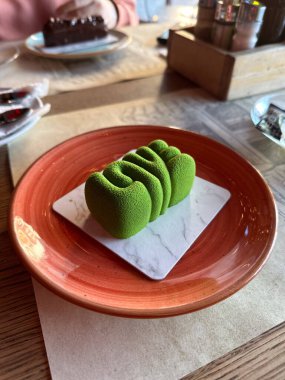 Kafe ortamında aynı yeşil aşk tatlısının yakın plan görüntüsü. Ilık ışıklandırma ve bulanık arkaplan rahat bir atmosfer ekler.