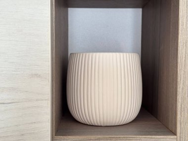 Ahşap bir rafta seramik vazo sergileniyor. Temiz ve desenli yüzey iç dekorasyon için çağdaş ama zamansız bir tasarım sunuyor.