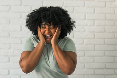 Afro saç stili ve espiri anlayışı olan gülen Afro-Amerikalı bir kadın. Arka plandaki tuğla duvarda gülüyor ve gülümsüyor. Mutluluk ve iyi duygular