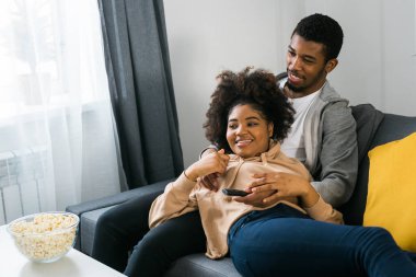 Mutlu Afrikalı Amerikalı çift televizyon izlerken birlikte kaliteli zaman geçirmekten hoşlanıyor. Kanepeye yakın oturan erkek ve kadın rahat bir yuva ortamında rahatlık ve iletişim gösteriyorlar. TV, dizi