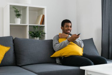 Neşeli kıvırcık saçlı, hafta sonu televizyon ya da film izlerken rahat bir kanepede dinlenen gündelik giysili Afro-Amerikan erkeği. Televizyon seti, çevrimiçi televizyon ve işletme