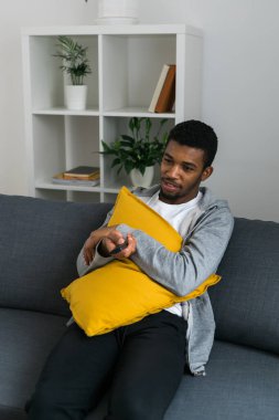 Neşeli kıvırcık saçlı, hafta sonu televizyon ya da film izlerken rahat bir kanepede dinlenen gündelik giysili Afro-Amerikan erkeği. Televizyon seti, çevrimiçi televizyon ve işletme