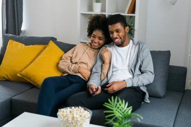 Mutlu Afrikalı Amerikalı çift televizyon izlerken birlikte kaliteli zaman geçirmekten hoşlanıyor. Kanepeye yakın oturan erkek ve kadın rahat bir yuva ortamında rahatlık ve iletişim gösteriyorlar. TV, dizi