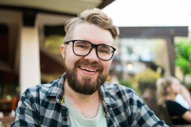 Gözlüklü sakallı adam dışarıda bir kafede otururken neşeyle gülüyor.