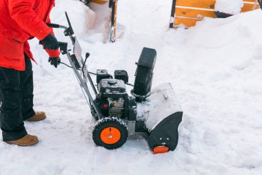 Closeup of red snow blower in action. Senior mature man outdoor in front of house using snowblower machine for removing snow on yard. Snow thrower in winter outside home. Young worker guy blowing snow