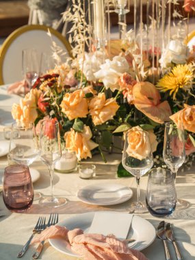 Düğün. Ziyafet. Konuklar, yuvarlak masa ve sandalyeler çatal bıçak takımı, çiçekler ve çanak çömlek ile servis ve bir masa örtüsü ile kaplı