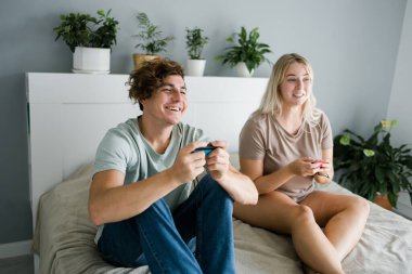 Genç çift yatak odasındaki yatakta yatarken video oyunu oynuyorlar, hafta sonları eğleniyorlar ve eğleniyorlar. Teknoloji ve oyun konsepti.