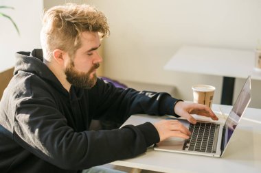 Kafeteryada dinlenen beyaz bir erkek sosyal ağlarda sohbet ediyor yetenekli bir serbest yazar bilgisayarında web günlüğü için yazı yazmanın keyfini çıkarıyor.