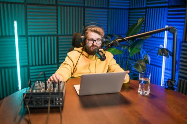 Neşeli genç adam stüdyoda podcast yapıyor. Kulaklığı ve mikrofonu olan kendine güvenen bir adam podcast kaydediyor. İnternet radyosunda konuşan mutlu adam.