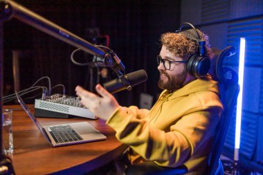 Neşeli genç adam stüdyoda podcast yapıyor. Kulaklığı ve mikrofonu olan kendine güvenen bir adam podcast kaydediyor. İnternet radyosunda konuşan mutlu adam.