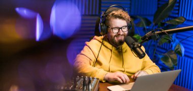 Genç gülümseyen erkek radyo sunucusu mikrofona konuşuyor ve haberleri, bilgileri ve iletişim kavramlarını okuyor. Podcast ve internet yayın kavramı