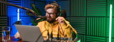 Genç gülümseyen erkek radyo sunucusu mikrofona konuşuyor ve haberleri, bilgileri ve iletişim kavramlarını okuyor. Podcast ve internet yayın kavramı