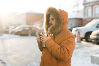 Şehrin güneşli kış sokağında elinde sıcak içki tutan bir adam. Soğuk kentsel yaşam tarzında sıcaklık, sükunet ve günlük açık hava rutini. Boşluğu kopyala