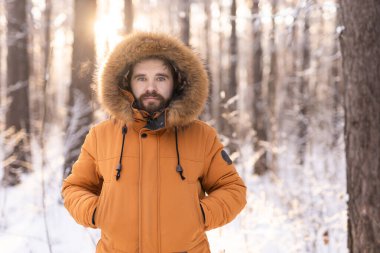 Kışlık ceketli bir adam gün doğumunda karlı ormanda duruyor. Yalnızlık, doğayla bağlantı ve sakin kış tefekkürleri. Boşluğu kopyala.