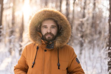 Kışlık ceketli bir adam gün doğumunda karlı ormanda duruyor. Yalnızlık, doğayla bağlantı ve sakin kış tefekkürleri. Boşluğu kopyala.