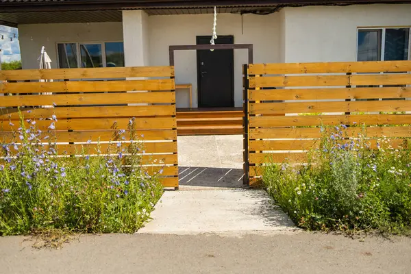 Kapı açık, evin önünde çiçekler olan ahşap çitler. Açık erişim, doğal sınır ve banliyö giriş tasarımı.