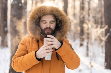 Adam, güneş doğarken karlı kış ormanlarında termostan içer. Yalnızlık, sıcaklık ve kış manzarasında barışçıl doğa rutini. Boşluğu kopyala.