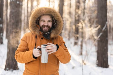 Adam, güneş doğarken karlı kış ormanlarında termostan içer. Yalnızlık, sıcaklık ve kış manzarasında barışçıl doğa rutini. Boşluğu kopyala.