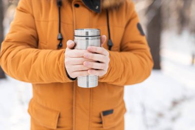 Adam kış sabahı karlı ormanda termos tutuyor. Soğuk bir mevsim boyunca sıcak çay, konfor ve farkındalık.
