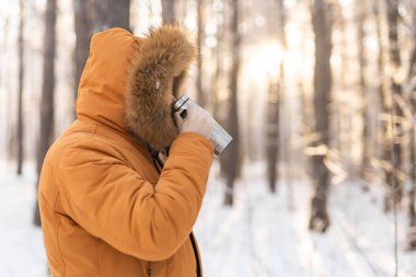 Adam, güneş doğarken karlı kış ormanlarında termostan içer. Yalnızlık, sıcaklık ve kış manzarasında barışçıl doğa rutini. Boşluğu kopyala.