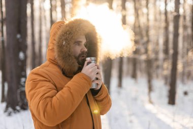 Adam karlı kış ormanlarında termosla ısınıyor. Soğuk doğal ortamda konfor ve sabah farkındalığı.