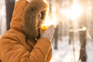 Karlı ormanda sarı bardaktan içen adam. Kışın hayatta kalmasını, günlük ritüelleri ve dışarıdaki sıcaklıkla farkındalık arasındaki bağlantıyı yansıtır.