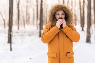 Karlı ormanda sarı kupalı bir adam kameraya bakıyor. Sessiz bir kış molası sırasında, farkındalık, sıcaklık ve doğayla olan insan ilişkileri.
