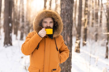 Karlı ormanda sarı kupalı bir adam kameraya bakıyor. Sessiz bir kış molası sırasında, farkındalık, sıcaklık ve doğayla olan insan ilişkileri.