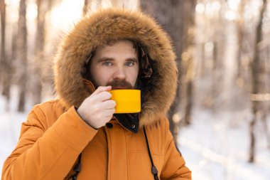 Karlı ormanda sarı kupalı bir adam kameraya bakıyor. Sessiz bir kış molası sırasında, farkındalık, sıcaklık ve doğayla olan insan ilişkileri.