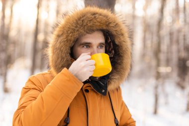 Karlı ormanda sarı kupalı bir adam kameraya bakıyor. Sessiz bir kış molası sırasında, farkındalık, sıcaklık ve doğayla olan insan ilişkileri.