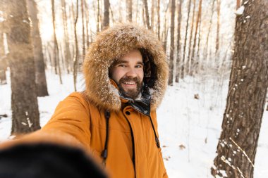 Karlı ormanda neşeli bir kış selfie 'si çeken bir adam. Mutluluk, macera ve soğuk bir mevsimde doğanın güzelliğinin tadını çıkarmak..