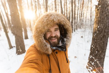 Karlı ormanda neşeli bir kış selfie 'si çeken bir adam. Mutluluk, macera ve soğuk bir mevsimde doğanın güzelliğinin tadını çıkarmak..
