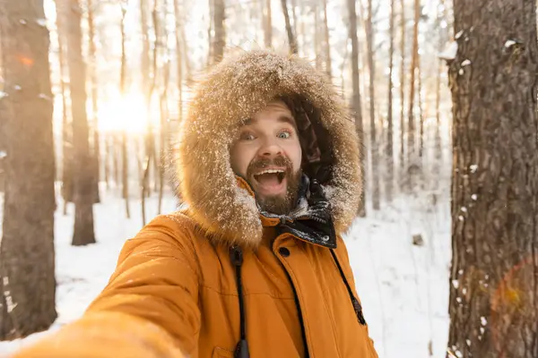 Orman yürüyüşü ve selfie çekmekten zevk alan heyecanlı bir adam. Kar mevsiminde neşe, özgürlük ve doğa ile bağlantı
