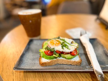 Samimi bir kafede seramik tabakta servis edilen yumurtalı avokado tostu. Sağlıklı kahvaltı ve dengeli beslenme.