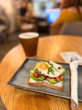 Samimi bir kafede seramik tabakta servis edilen yumurtalı avokado tostu. Sağlıklı kahvaltı ve dengeli beslenme.